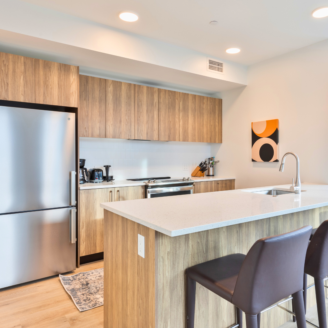 Modern kitchen featuring stainless steel appliances, wooden cabinetry, and a minimalist countertop with bar stools.