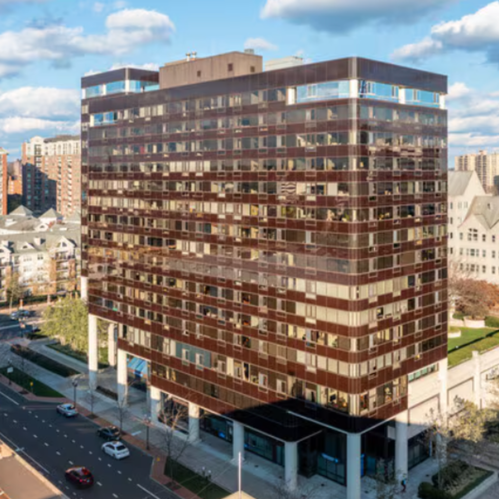 Exterior view of a modern brownstone building with large windows and balconies, situated in a city environment.